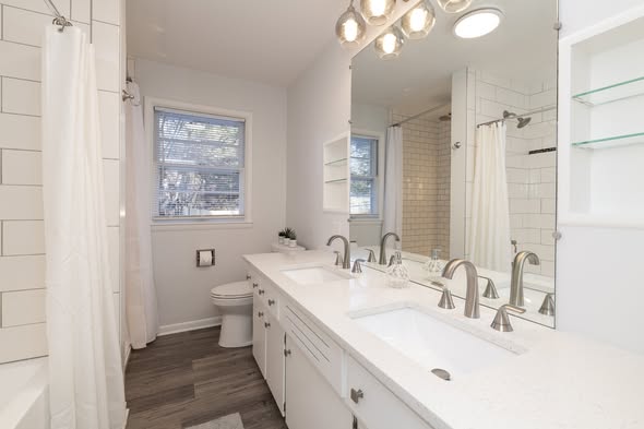 Finished bathroom with a long white double vanity, twin mirrors and a tiled shower beyond