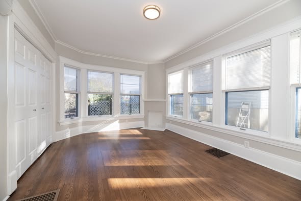 Finished sunroom with white walls, wraparound windows and hardwood flooring